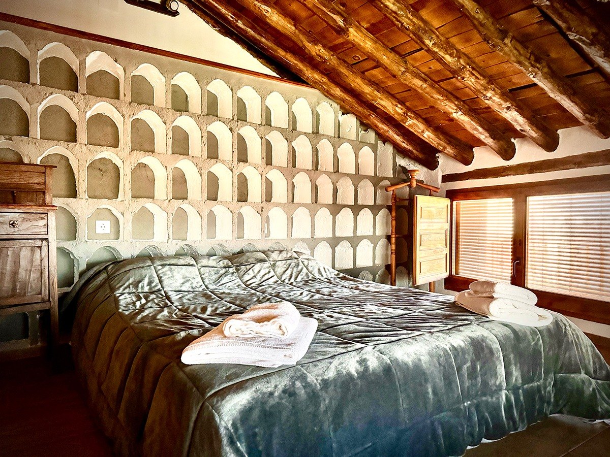 Dormitorio abuhardillado con cama doble y vigas de madera en Las Grullas Casa Rural