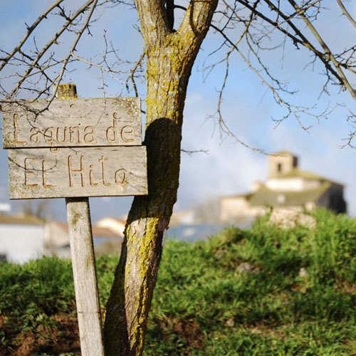 Cartel de madera de la Laguna de El Hito con el pueblo al fondo